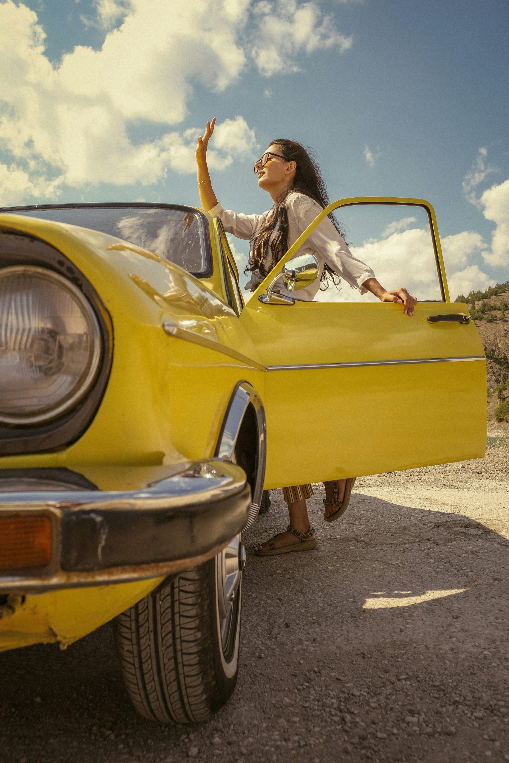 Woman standing by a yellow vintage car with the door open, enjoying a sunny day.